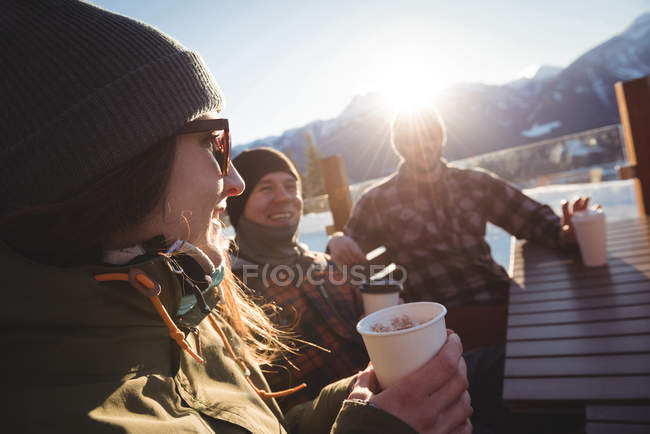 Esquiadores amigos interagindo uns com os outros enquanto toma xícaras de café em estância de esqui — Fotografia de Stock