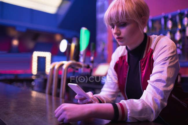 Garçonete feminino usando telefone celular no balcão no bar — Fotografia de Stock