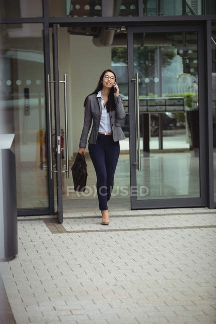 Деловая женщина, идущая во время разговора по мобильному телефону возле офисного здания — стоковое фото