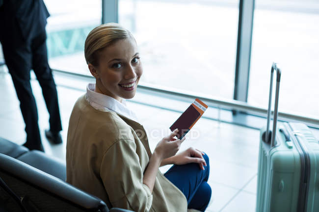 Portrait d'une passagère avec passeport et carte d'embarquement dans la salle d'attente de l'aéroport — Photo de stock