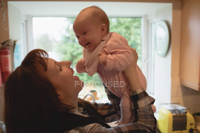 Мати грає зі усміхненою дитиною на кухні вдома — стокове фото