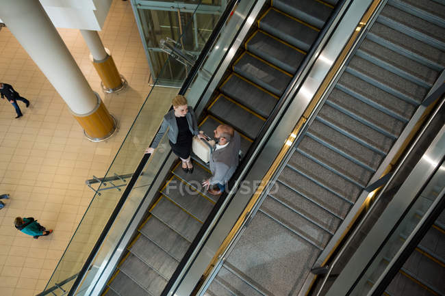 Geschäftsleute interagieren miteinander, während sie auf der Rolltreppe am Flughafen-Terminal nach unten fahren — Stockfoto