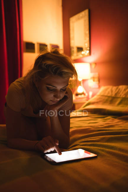 Mulher deitada e usando tablet digital na cama no quarto — Fotografia de Stock