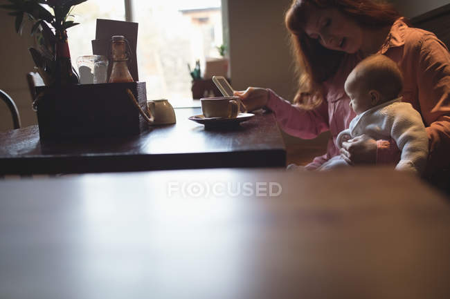 Средняя взрослая женщина с маленькой дочерью с помощью мобильного телефона в кафе — стоковое фото