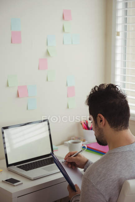 Hombre atento escribiendo en el documento mientras está sentado en el escritorio - foto de stock