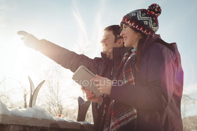 Skier couple with digital tablet looking at a distance in ski resort — Stock Photo