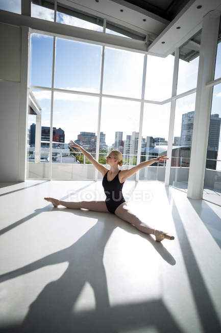 Ballerine s'étirant sur le sol tout en pratiquant la danse de ballet au studio — Photo de stock