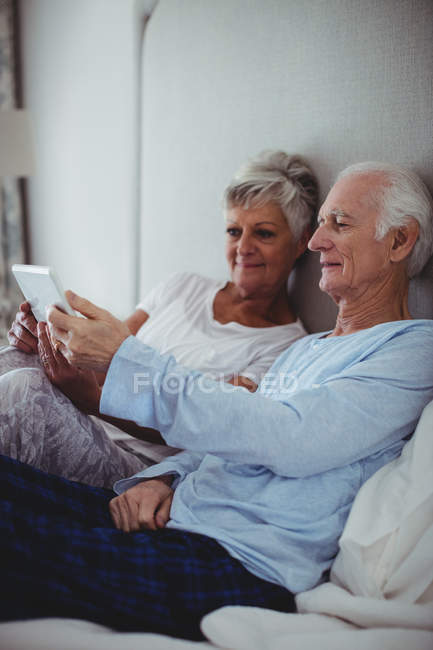 Couple aîné utilisant une tablette numérique sur le lit dans la chambre à coucher — Photo de stock