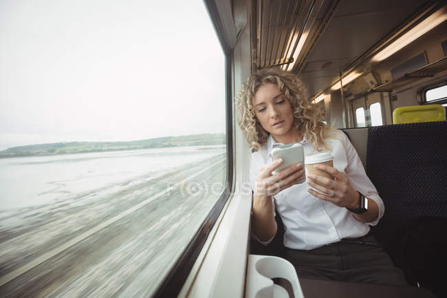 Взрослая деловая женщина с кофе, используя смартфон во время путешествия — стоковое фото