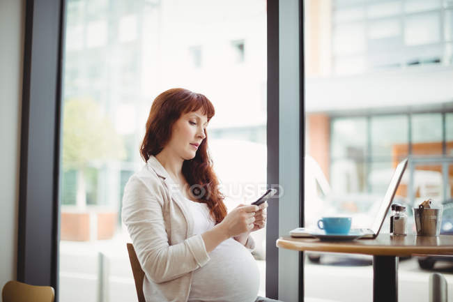 Pregnant businesswoman using mobile phone in office cafeteria — Stock Photo