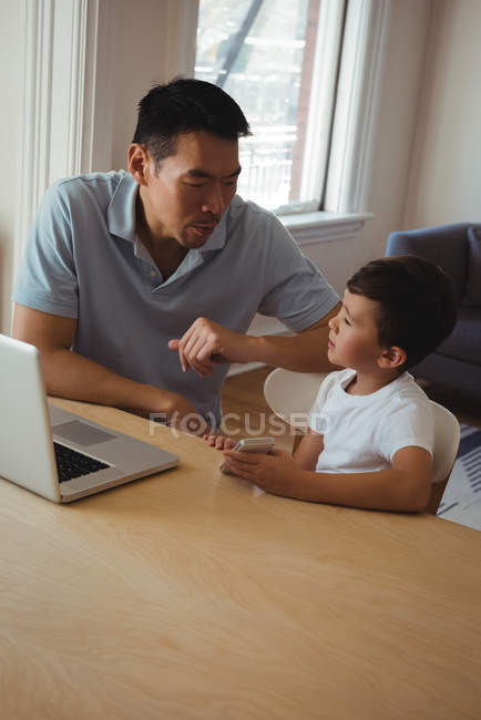 Father and son using mobile phone and laptop in living room at home — Stock Photo
