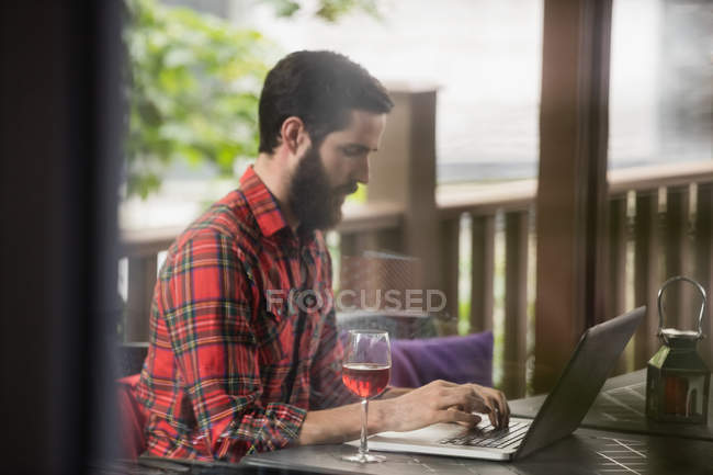 Человек с ноутбуком и бокалом вина на столе в баре — стоковое фото