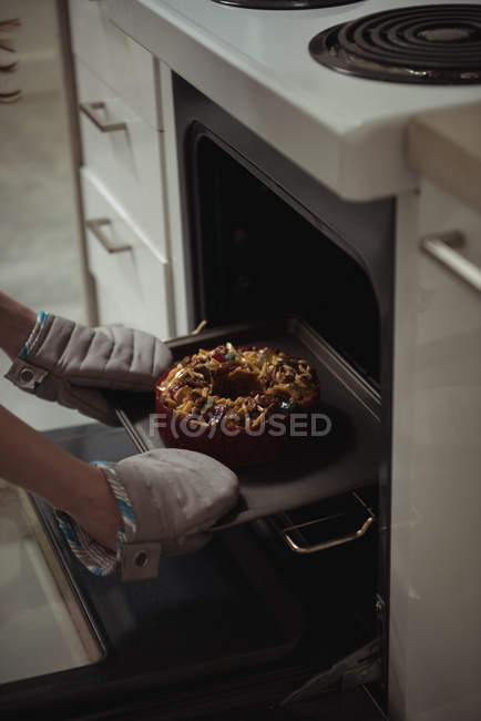 Close-up of woman in gloves removing baked cake from oven — Stock Photo