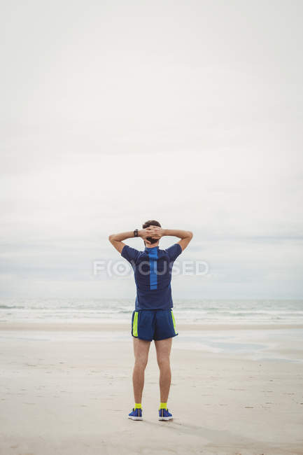 Athlet steht mit den Händen hinter dem Kopf am Strand — Stockfoto