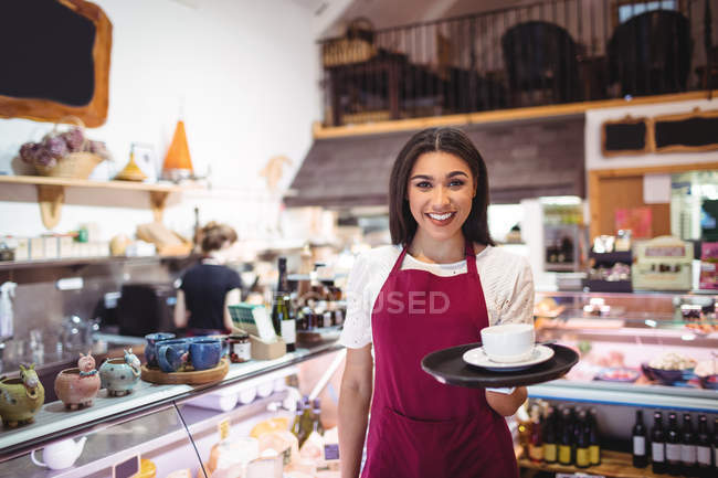 Портрет усміхненої офіціантки, що подає чашку кави за лічильником у супермаркеті — стокове фото