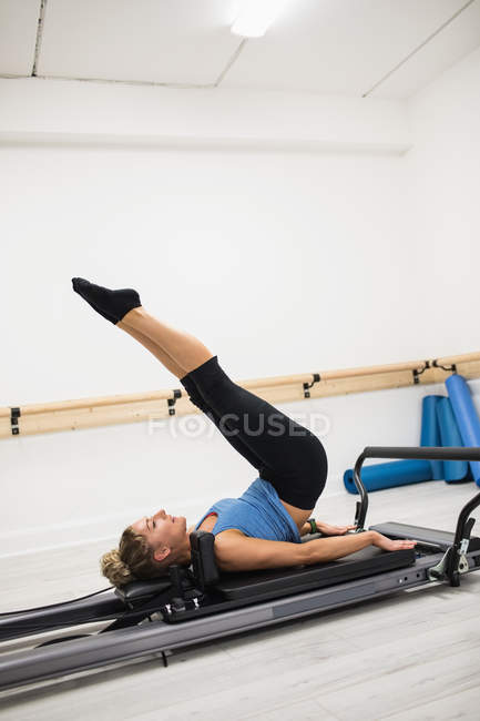 Femme faisant de l'exercice avec les pieds sur le réformateur dans la salle de gym — Photo de stock