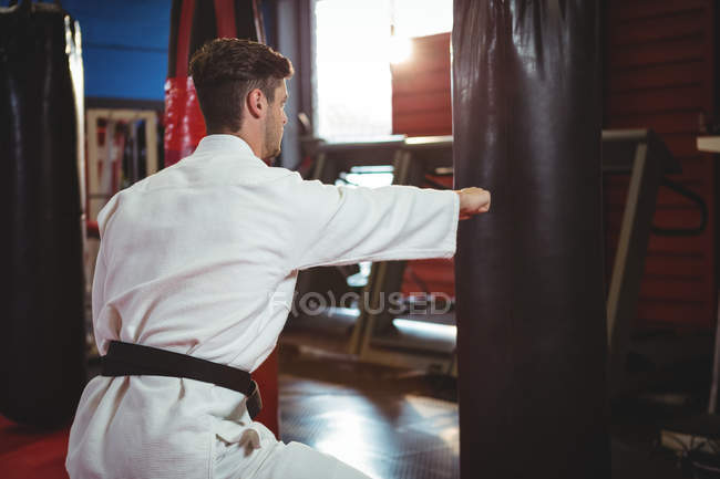 Karate player punching boxing bag in fitness studio — Stock Photo