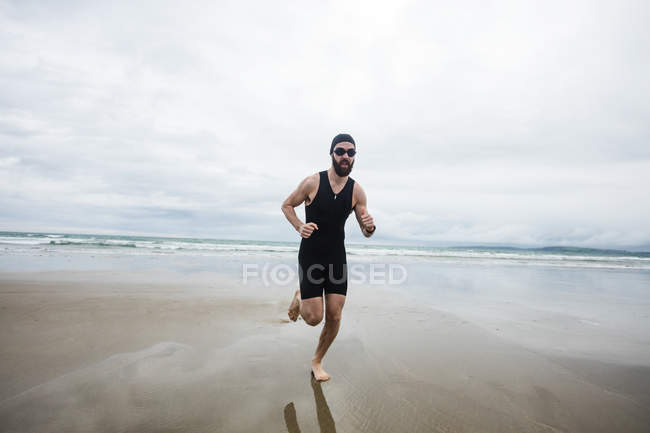 Мужчина в купальнике и плавательной шапочке бегает по пляжу — стоковое фото
