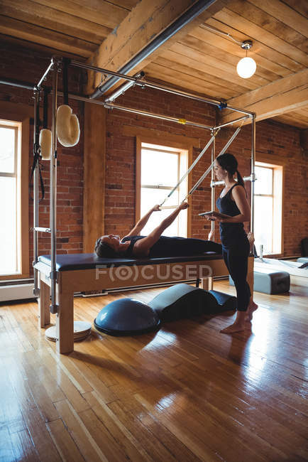 Instructor ayudando a la mujer mientras practica pilates en el gimnasio - foto de stock