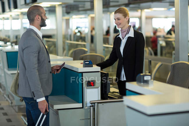 Lächelnder Pendler, der am Check-in-Schalter im Flughafenterminal mit dem Flugbegleiter interagiert — Stockfoto