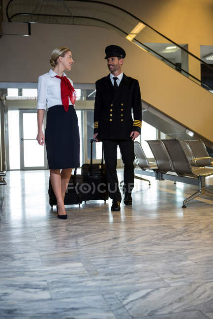 Piloto e aeromoça caminhando com seus sacos de carrinho no terminal do aeroporto — Fotografia de Stock