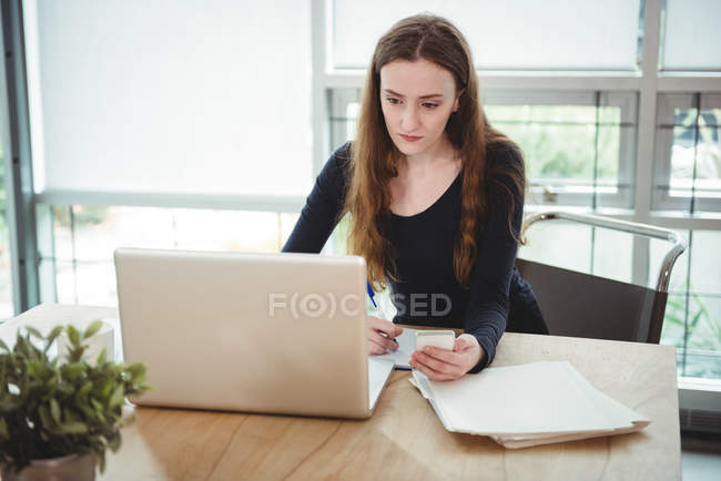 Executivo de negócios escrevendo no diário enquanto olha para laptop no escritório — Fotografia de Stock