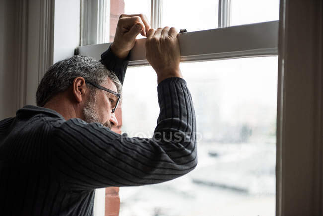Hombre reflexivo mirando a través de la ventana en casa - foto de stock