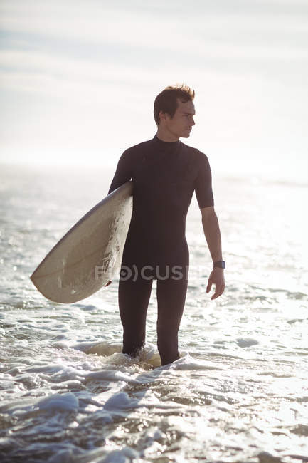 Задуманный серфер, стоящий с доской для серфинга в море — стоковое фото