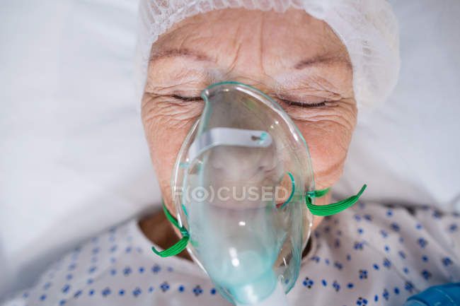 Close-up of senior patient wearing oxygen mask lying on hospital bed — Stock Photo