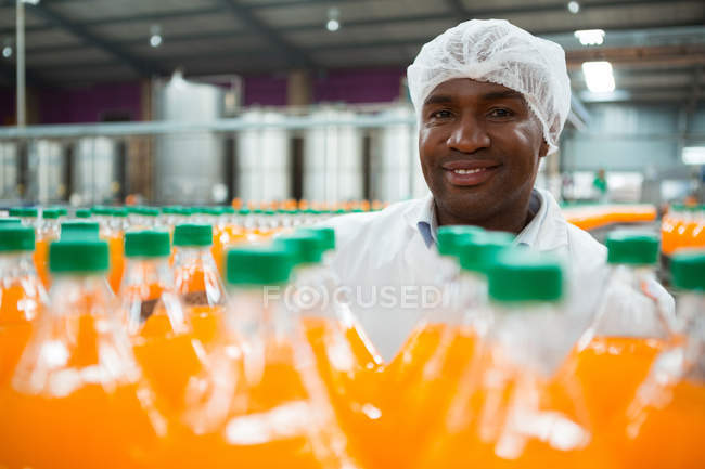Porträt eines glücklichen männlichen Arbeiters, der in einer Fabrik an Orangensaftflaschen steht — Stockfoto
