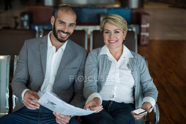 Retrato de gente de negocios sonriente sentada en la sala de espera con periódico en la terminal del aeropuerto - foto de stock