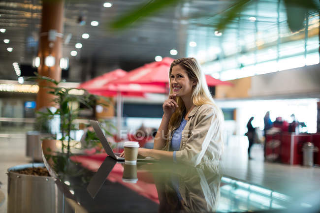 Hermosa mujer usando el ordenador portátil en la zona de espera en la terminal del aeropuerto - foto de stock