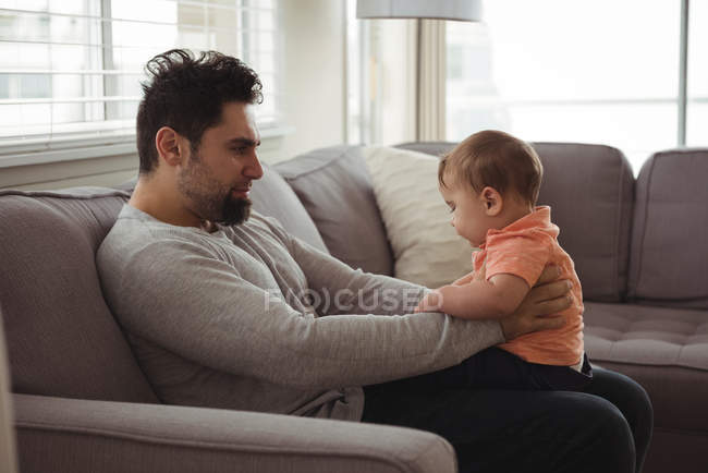 Pai brincando com seu bebê no sofá na sala de estar em casa — Fotografia de Stock