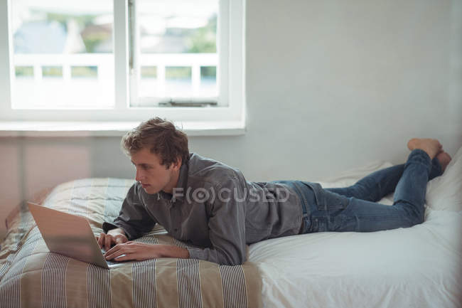 Uomo sdraiato sul letto e utilizzando il computer portatile a casa — Foto stock
