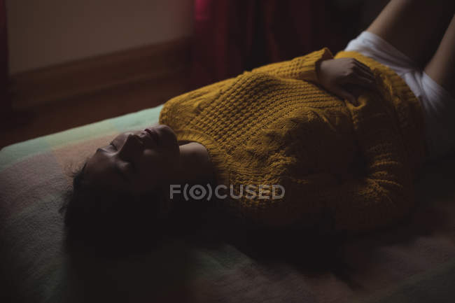 Femme orientale en pull jaune dormant sur le lit à la maison — Photo de stock