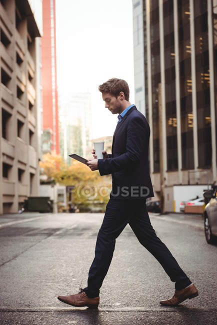 Homme d'affaires utilisant une tablette numérique tout en traversant la rue urbaine — Photo de stock