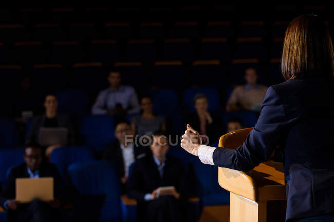 Vista trasera del ejecutivo femenino de negocios dando un discurso en el centro de conferencias - foto de stock