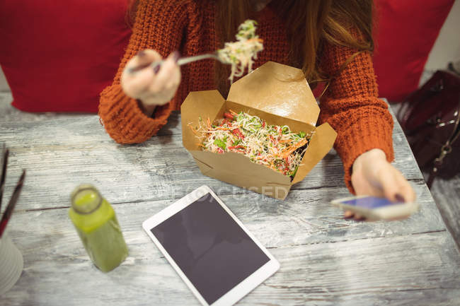 Високий кут зору жінки, використовуючи мобільний телефон під час їжі салат — стокове фото