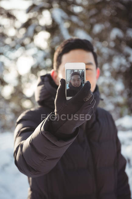 Homme souriant prenant selfie sur téléphone portable pendant l'hiver — Photo de stock