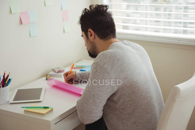 Уважний чоловік пише на документі, сидячи за столом — стокове фото