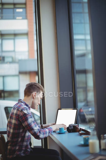 Молодий чоловік використовує ноутбук за лічильником в кафетерії — стокове фото