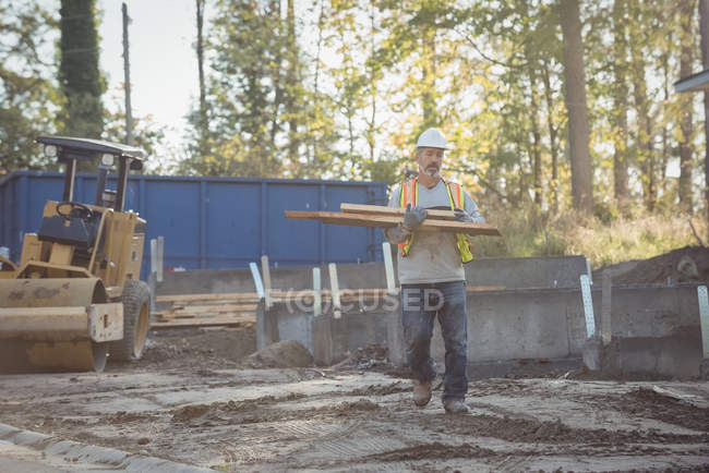 Будівельник, що перевозить деревину на будівельному майданчику — стокове фото