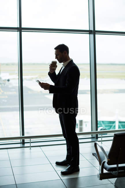 Бизнесмен пьет кофе во время использования цифрового планшета в зоне ожидания в аэропорту — стоковое фото