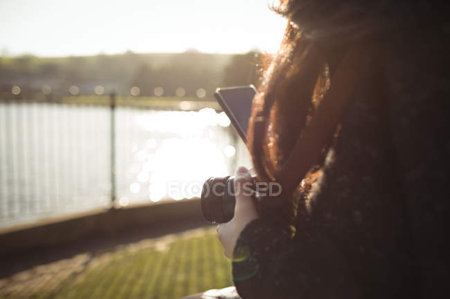 Крупный план женщины с помощью мобильного телефона во время хранения цифровой камеры — стоковое фото