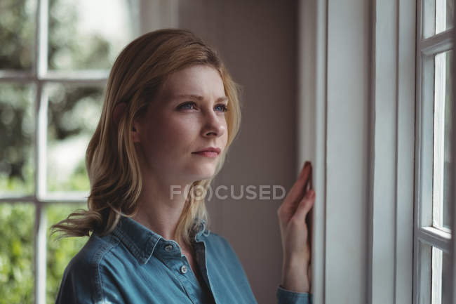 Femme réfléchie regardant par la fenêtre à la femme — Photo de stock