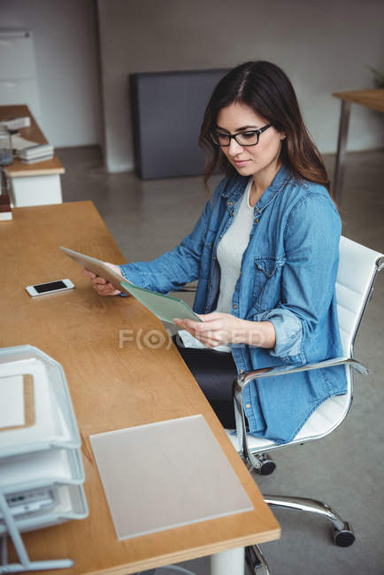 Business executive reading futuristic document and holding digital tablet in office — Stock Photo