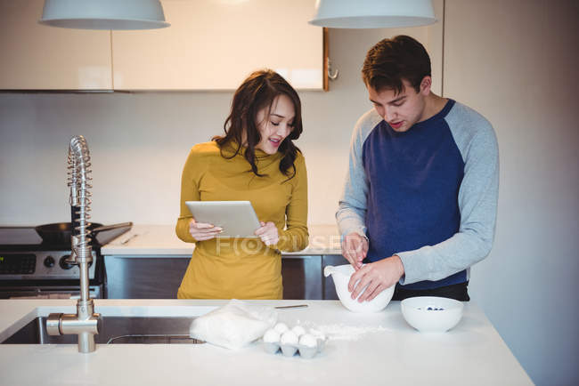 Пара с помощью цифрового планшета во время подготовки печенье на кухне дома — стоковое фото
