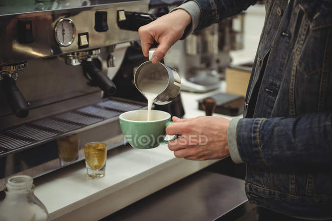 Sección media del hombre vertiendo leche en la taza de café en la cafetería - foto de stock