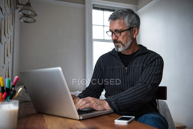 Uomo seduto a tavola e utilizzando il computer portatile a casa — Foto stock