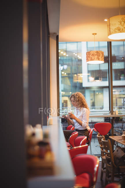 Blonde businesswoman sitting with coffee and smartphone at counter in cafeteria — Stock Photo